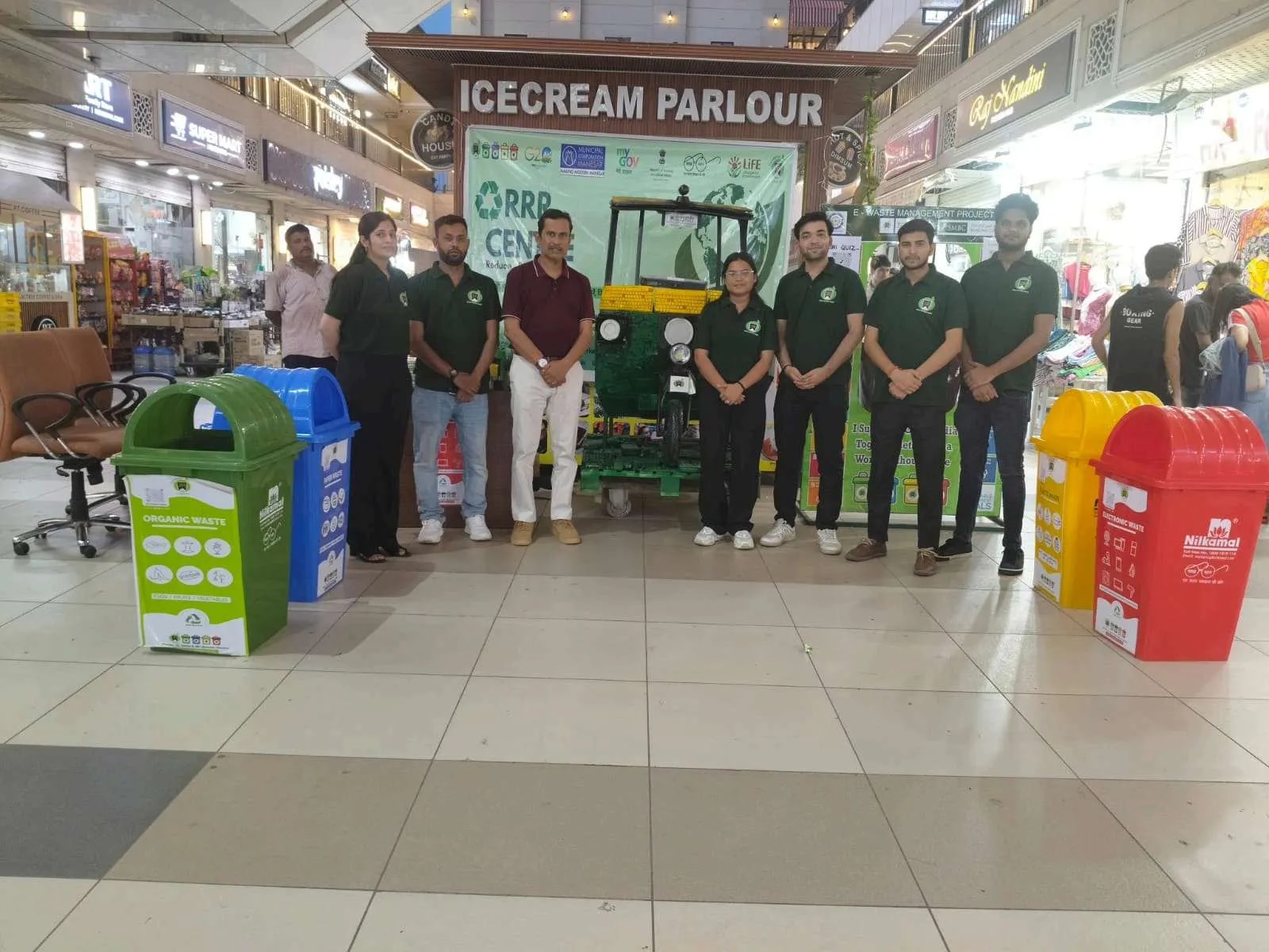 Team in green shirts in front of an RRR Centre with bins